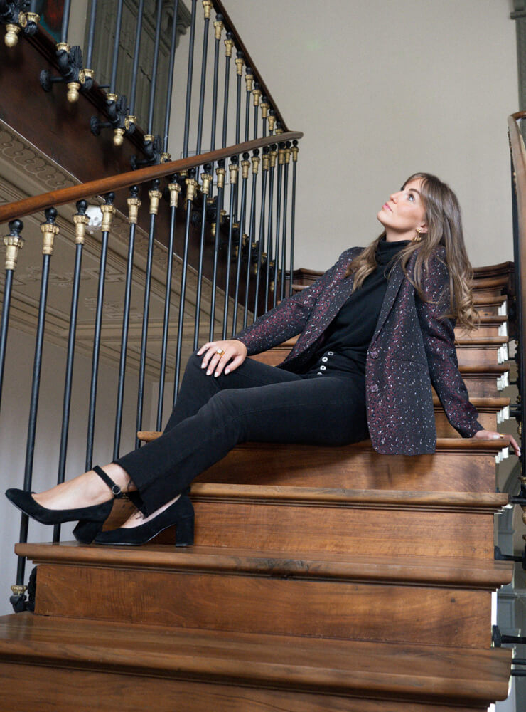 Modèle dans un escalier en bois qui porte une veste imprimé et jean noir June&River