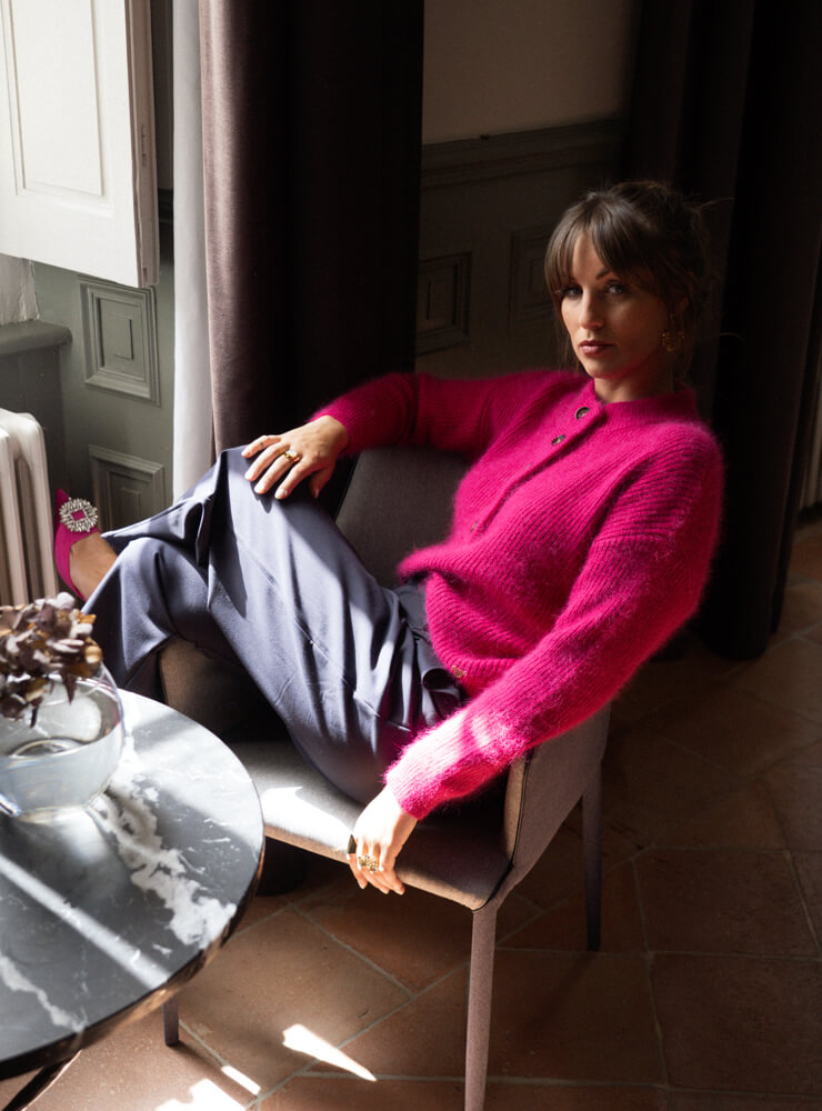 Modèle assis devant une fenêtre qui porte un pull rose et un pantalon bleu June&River