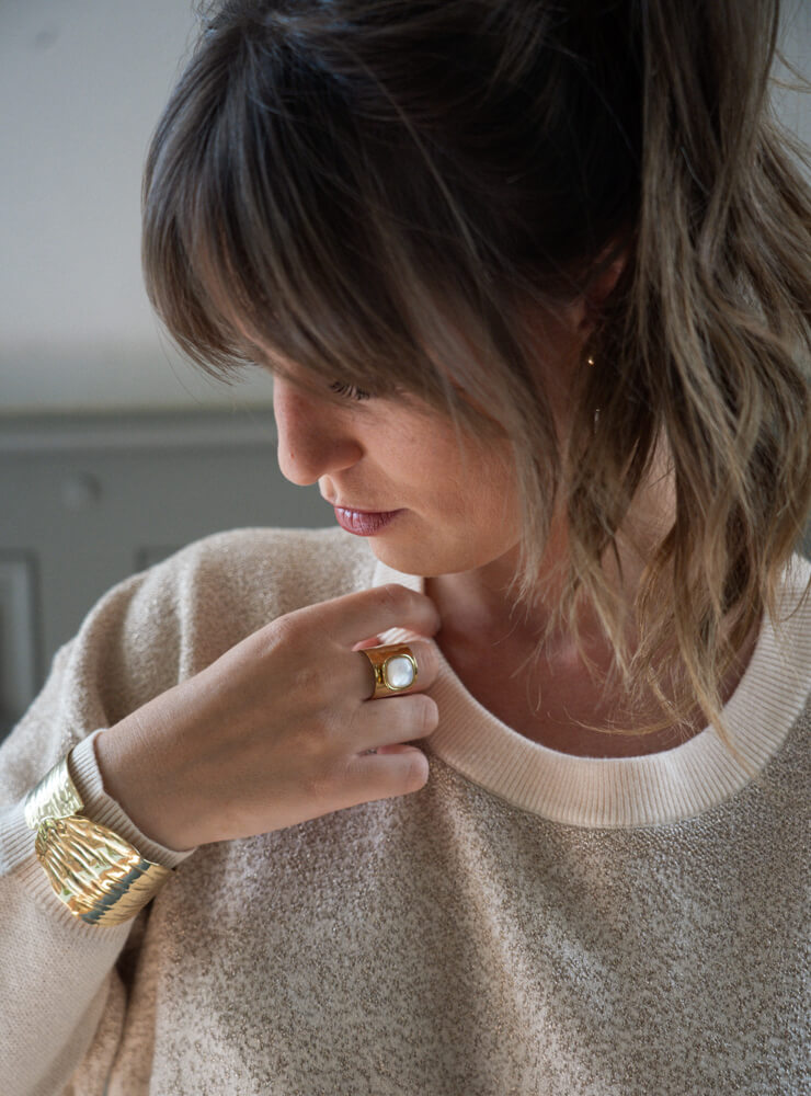 Modèle qui porte un pull beige et des bijoux June&River