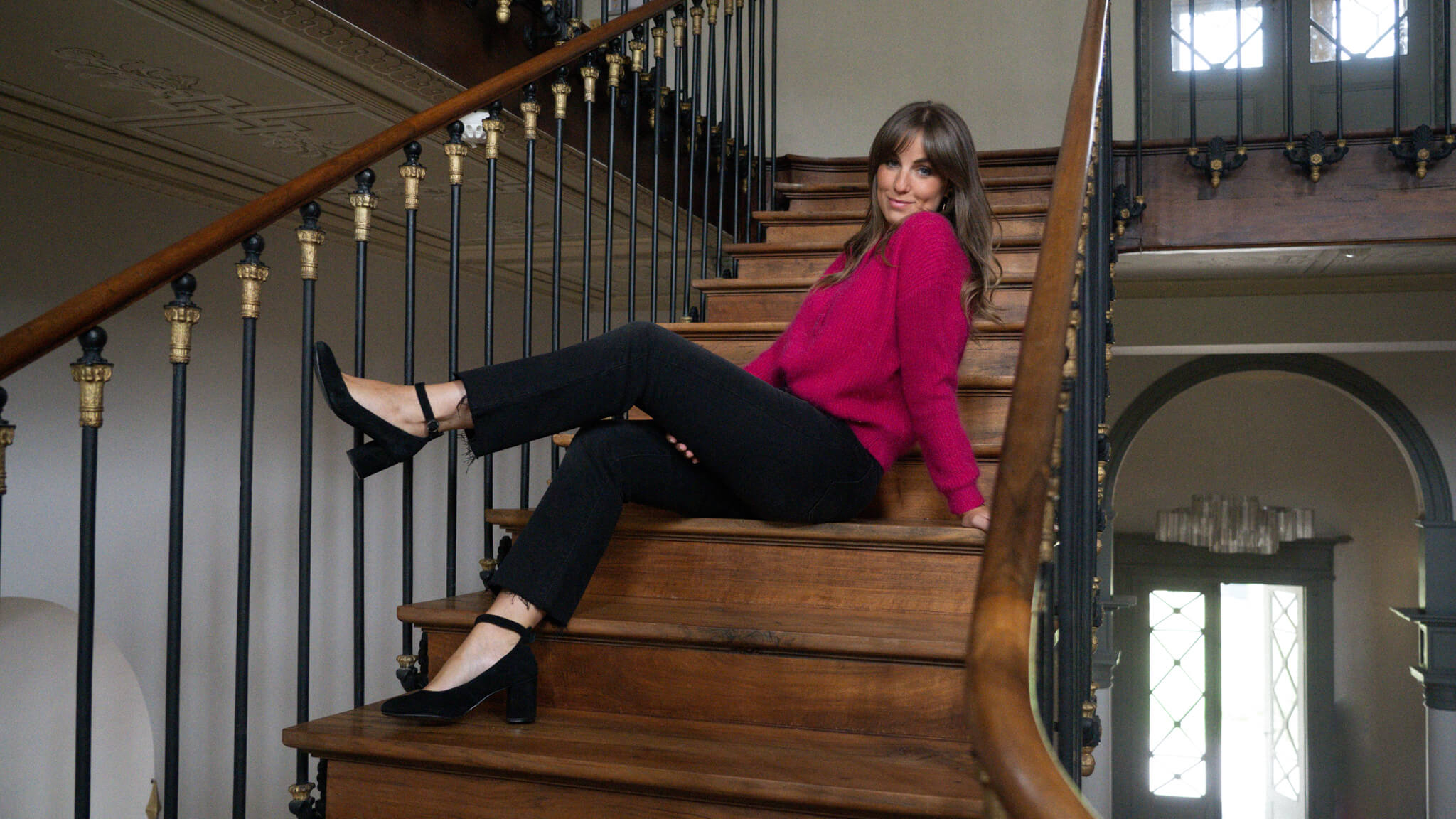 Modèle dans un escalier en bois qui porte un pull rose et un pantalon noir June&River