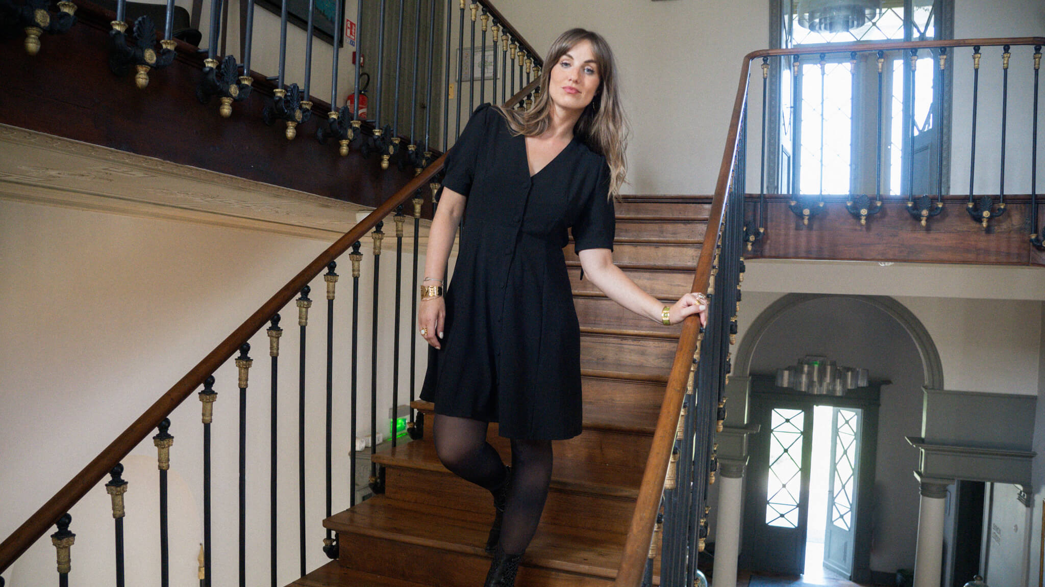 Modèle dans un escalier en bois qui porte une robe noire June&River