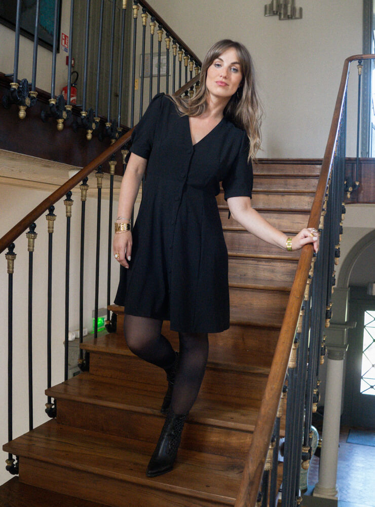 Modèle dans un escalier en bois qui porte une robe noire et des bijoux June&River
